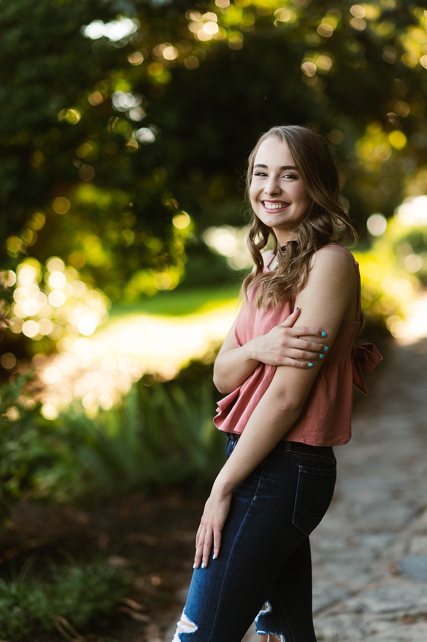 Woman in dusty pink tank top and jeans standing in park by Hannah Louise Photography