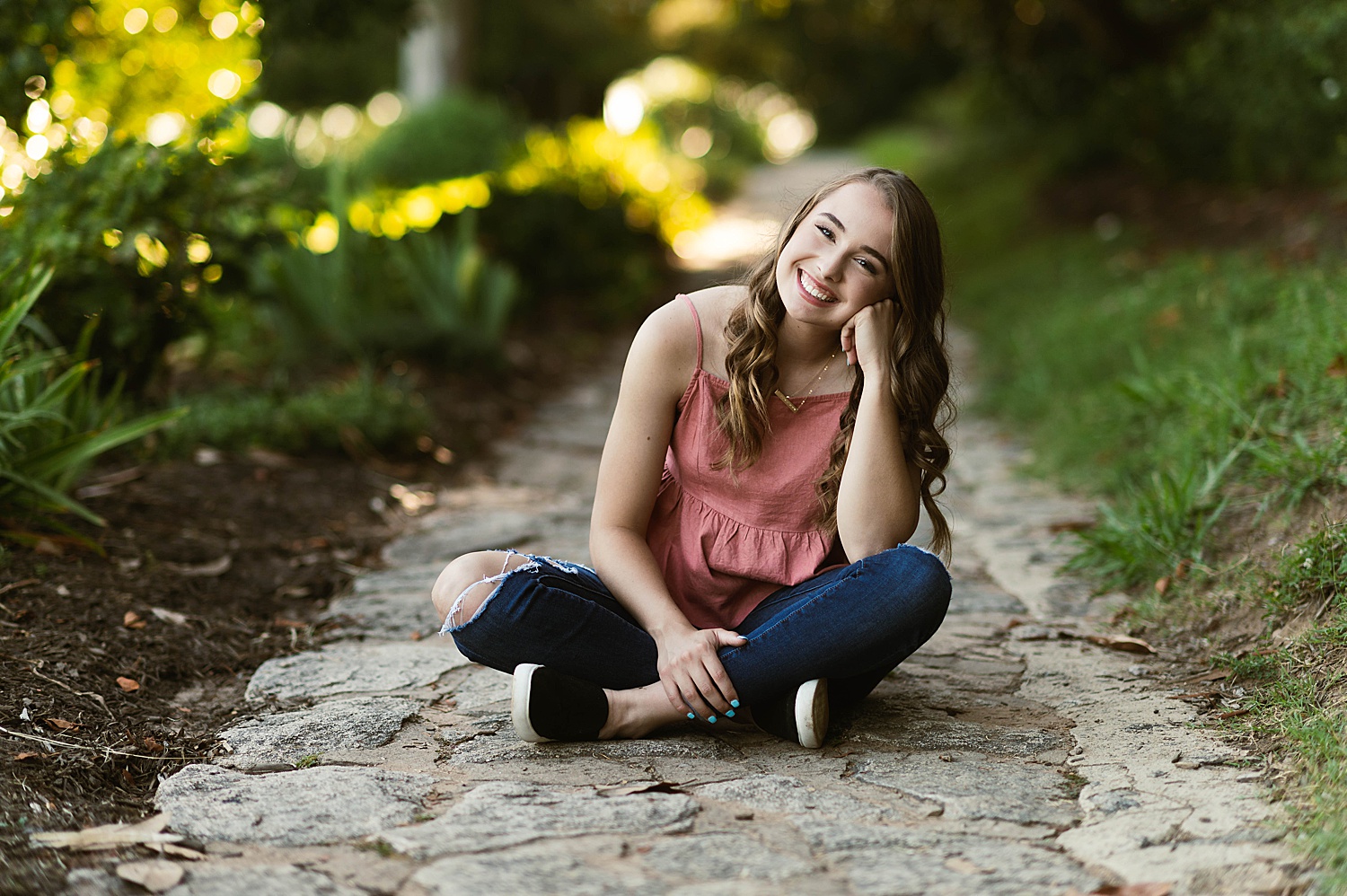 Girl in jeans and rose colored top sitting on pathway for Golden Hour Session 