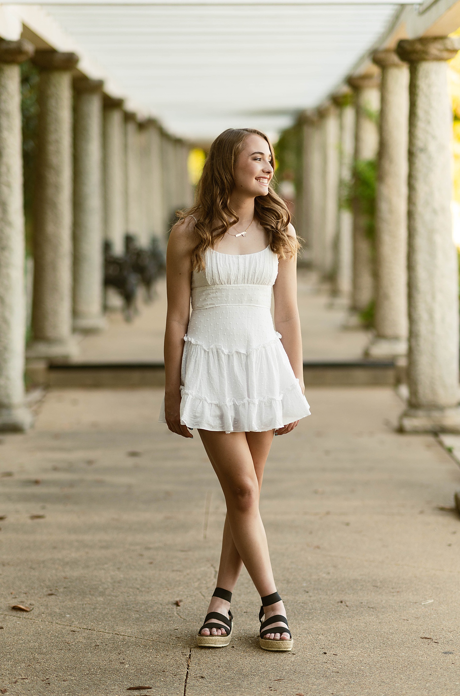Woman in white dress and gold jewelry standing by columns by Hannah Louise Photography