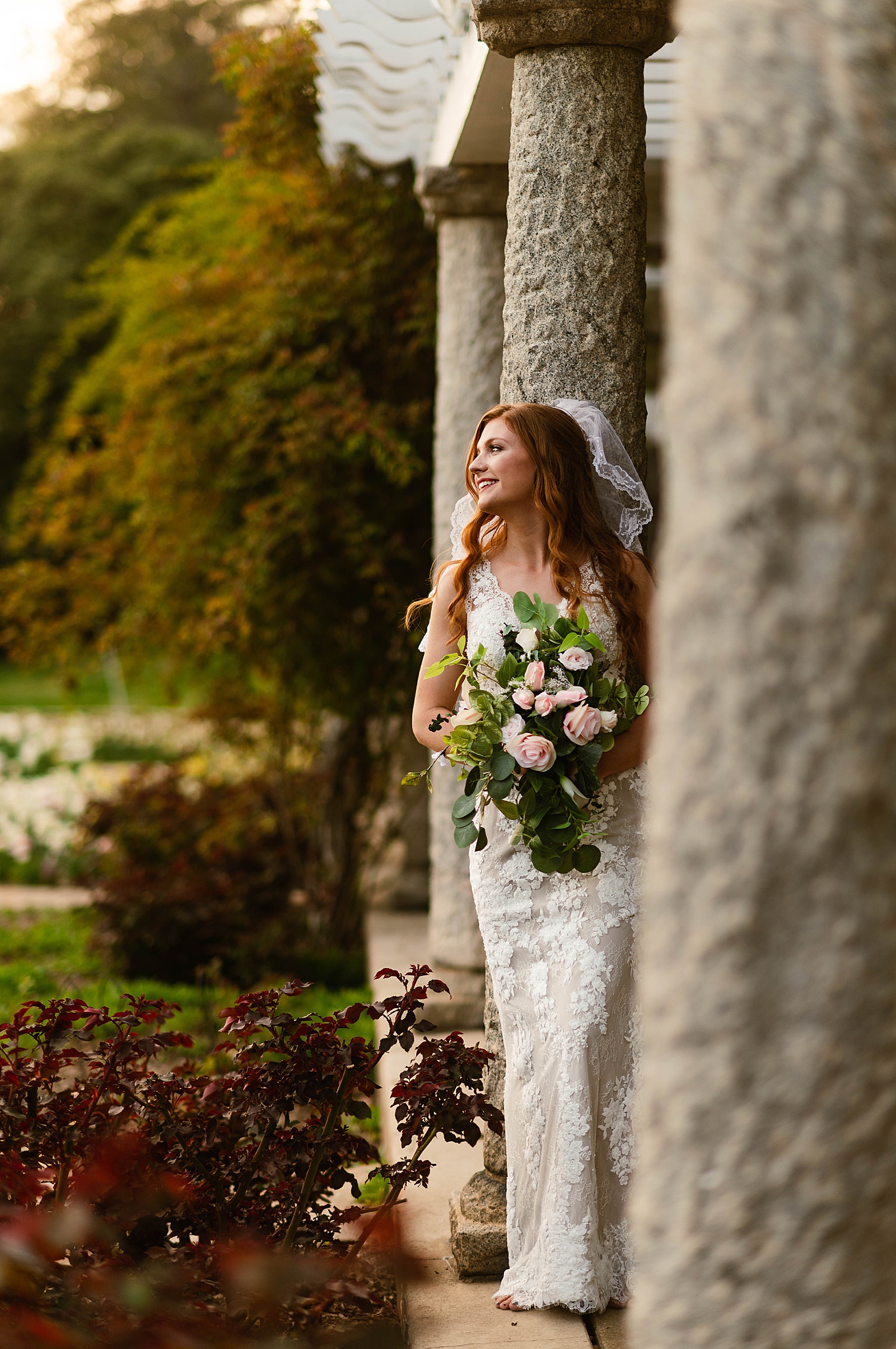 Woman with lace gown and bouquet leaning against column  by Hannah Louise Photo