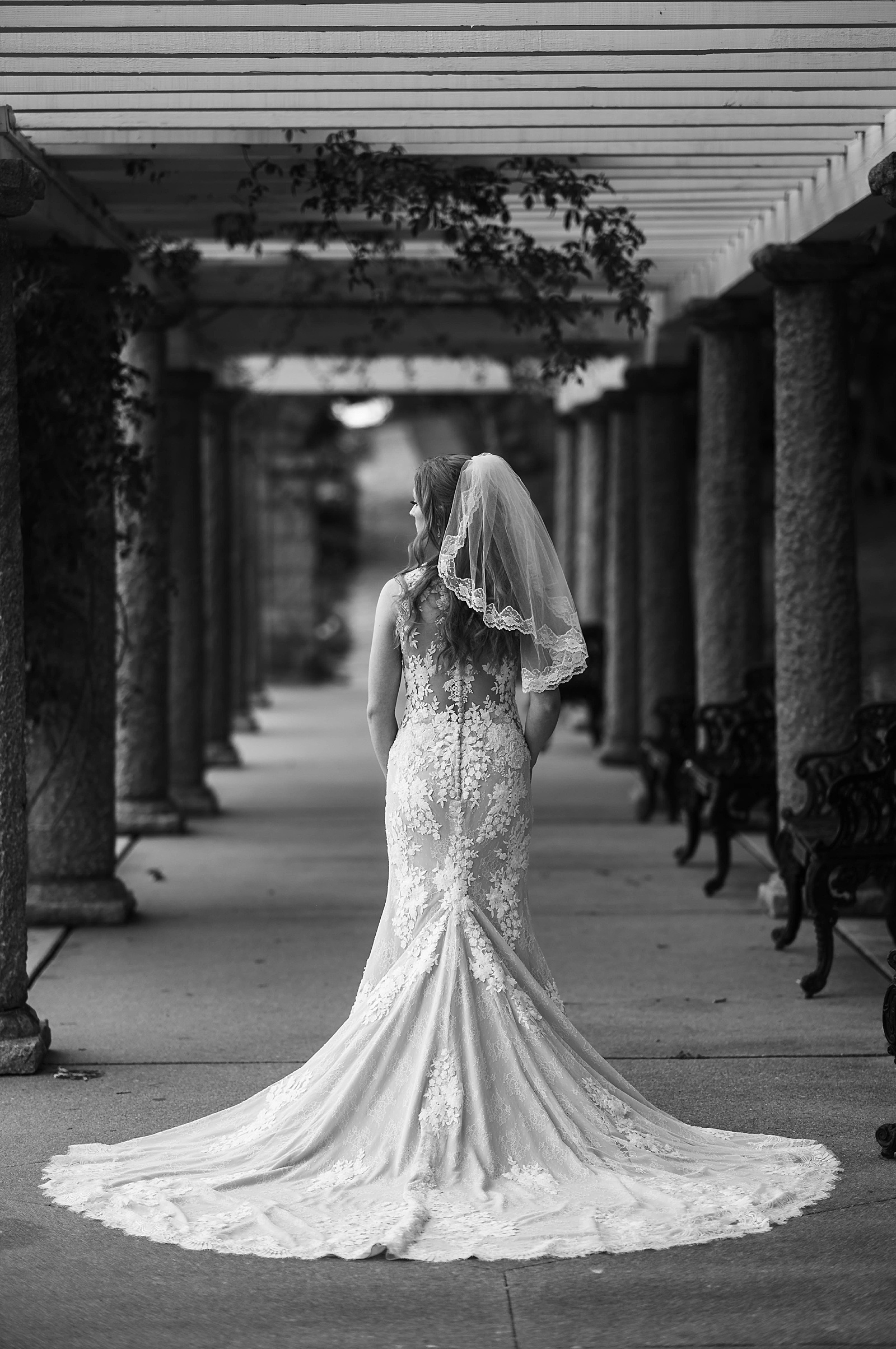 Bride in lace gown with train standing under columns by Richmond Elopement Photographer