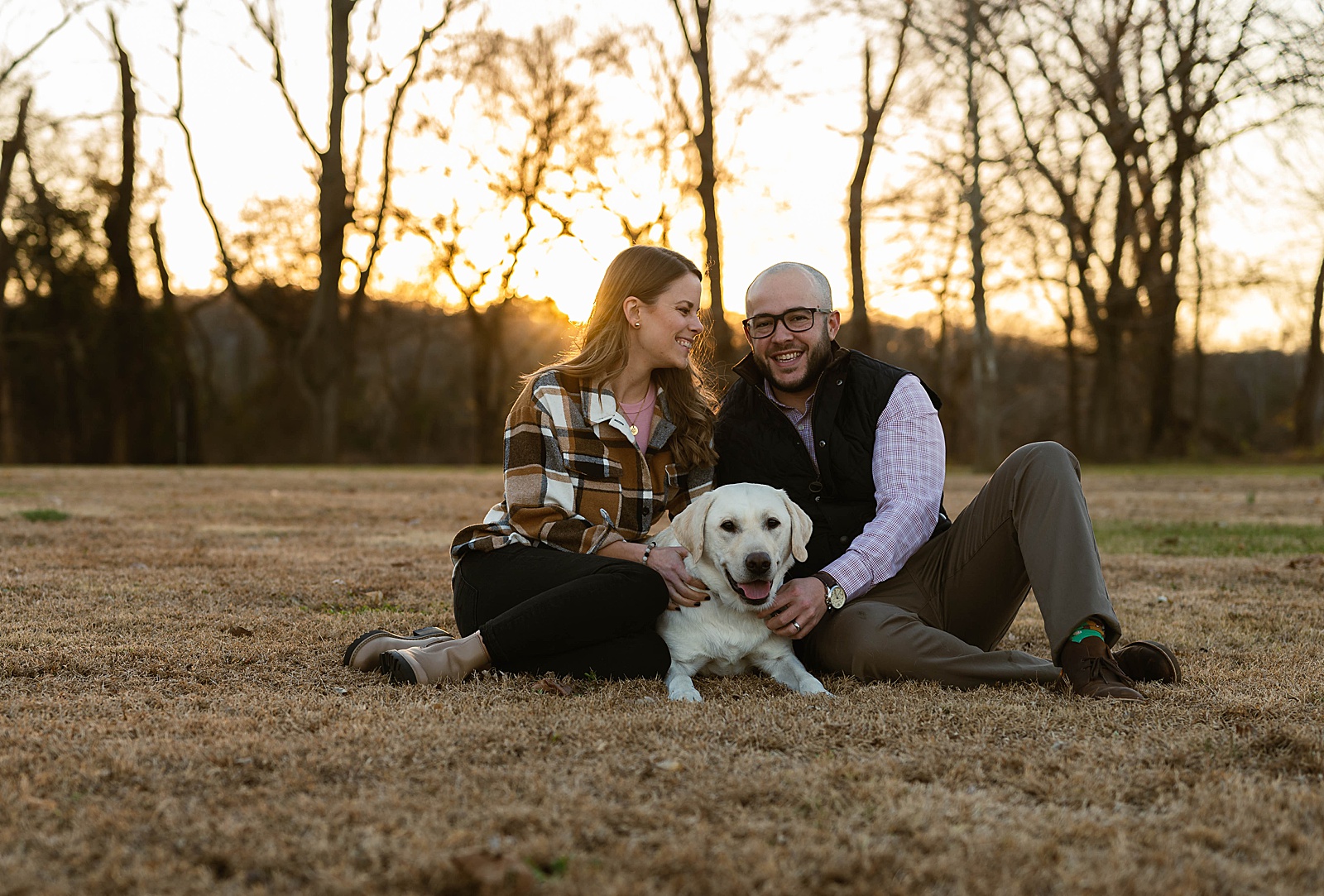 Married couple sitting with their dog at golden hour for holiday photos 